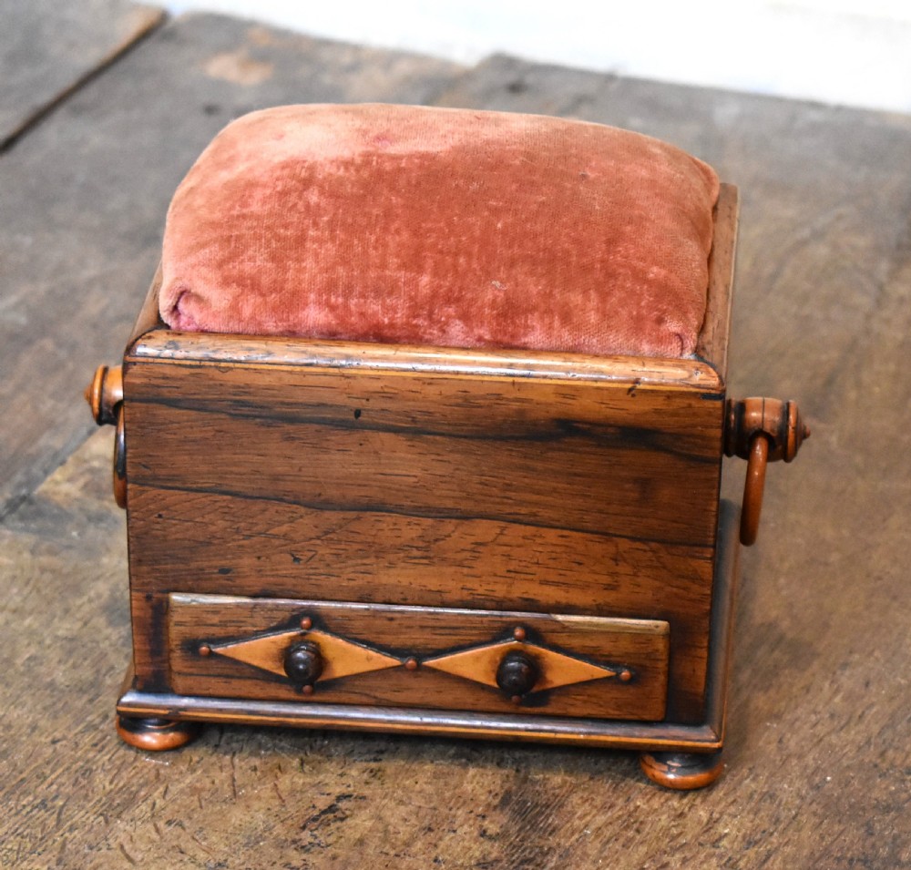 A small rectangular rosewood workbox featuring a terracotta velvet pincushion top, side handles, turned feet, and a drawer with inlaid diamond motifs.