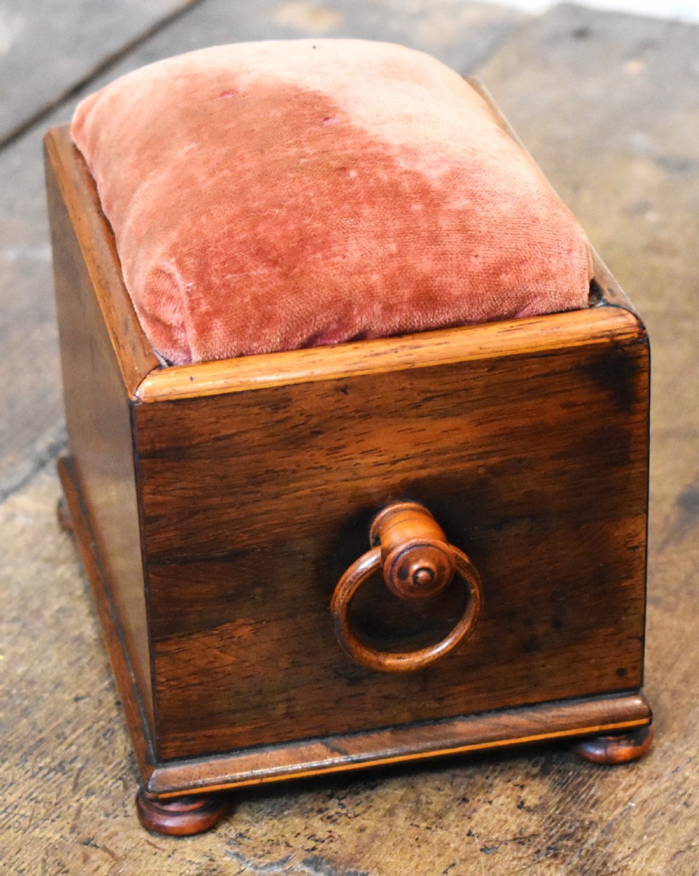 A small rectangular rosewood workbox featuring a terracotta velvet pincushion top, side handles, turned feet, and a drawer with inlaid diamond motifs. View VI