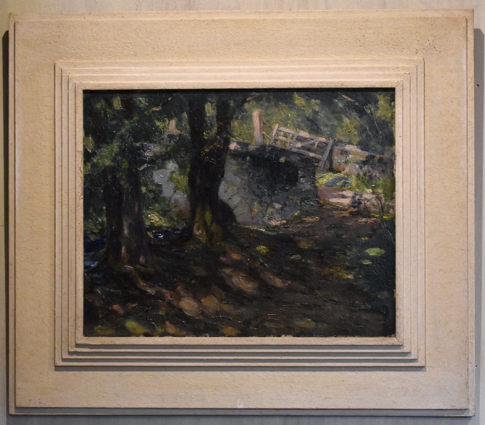 An oil painting depicting a dark woodland scene with trees, a stone bridge, and a wooden gate, housed within a textured off-white stepped frame. View II
