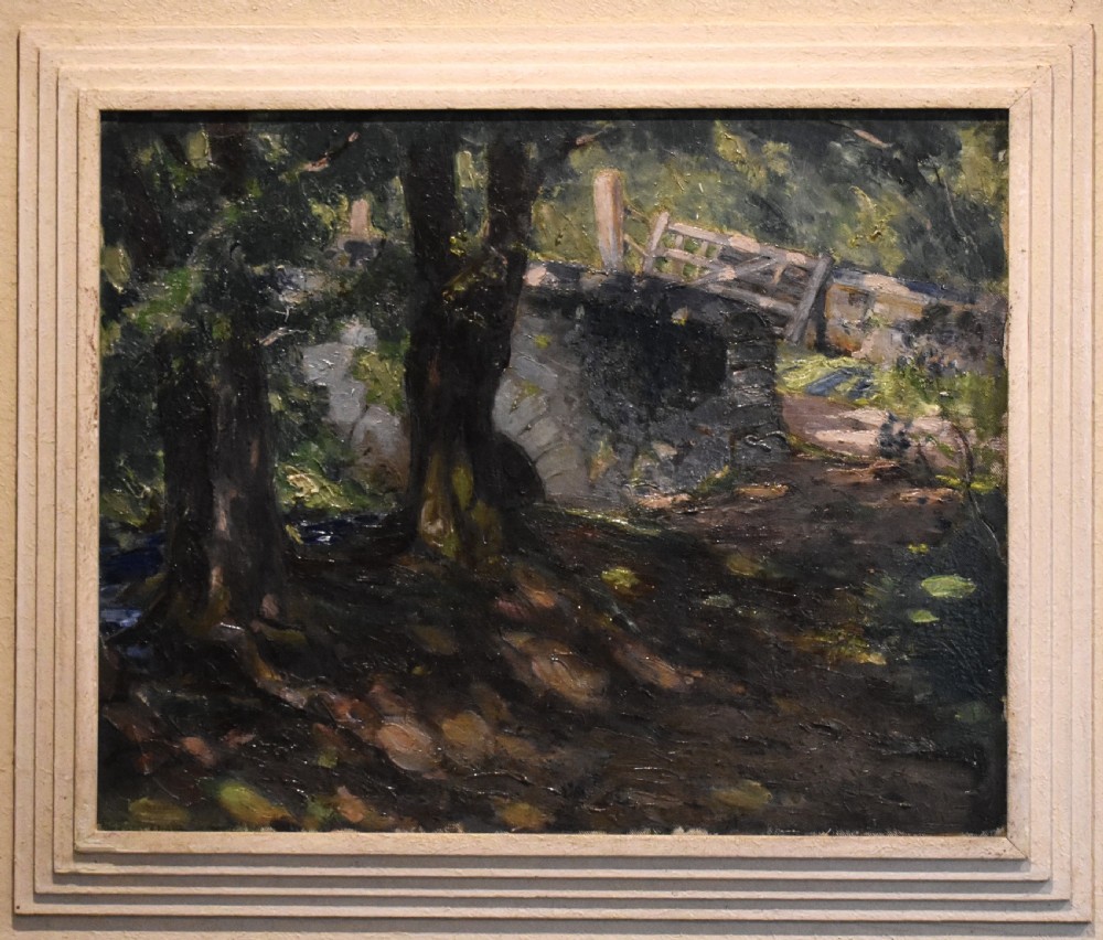 An oil painting depicting a dark woodland scene with trees, a stone bridge, and a wooden gate, housed within a textured off-white stepped frame. View V
