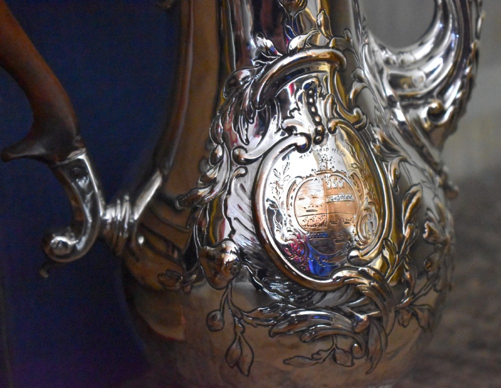 An antique Georgian silver-plated coffee pot featuring repousse floral scrollwork, an engraved cartouche, a carved wooden handle, and a finial lid. View II