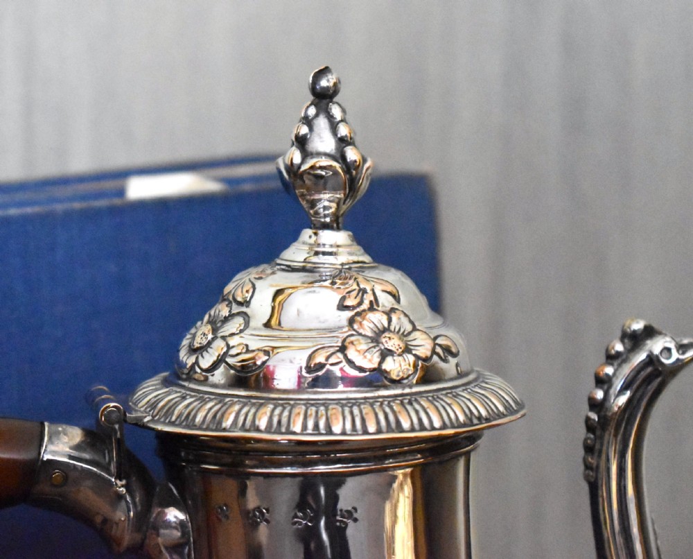 An antique Georgian silver-plated coffee pot featuring repousse floral scrollwork, an engraved cartouche, a carved wooden handle, and a finial lid. View III
