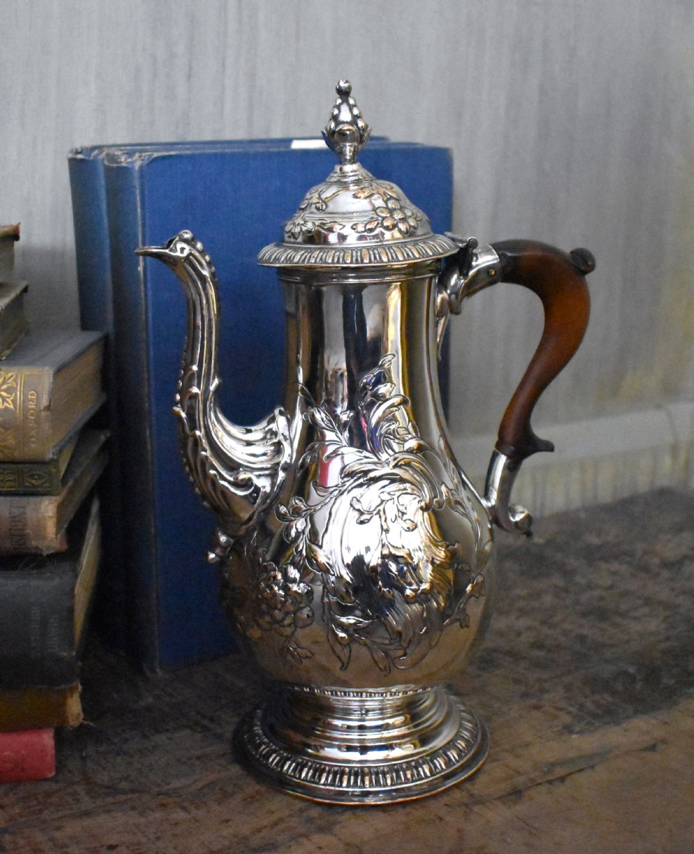 An antique Georgian silver-plated coffee pot featuring repousse floral scrollwork, an engraved cartouche, a carved wooden handle, and a finial lid. View VI
