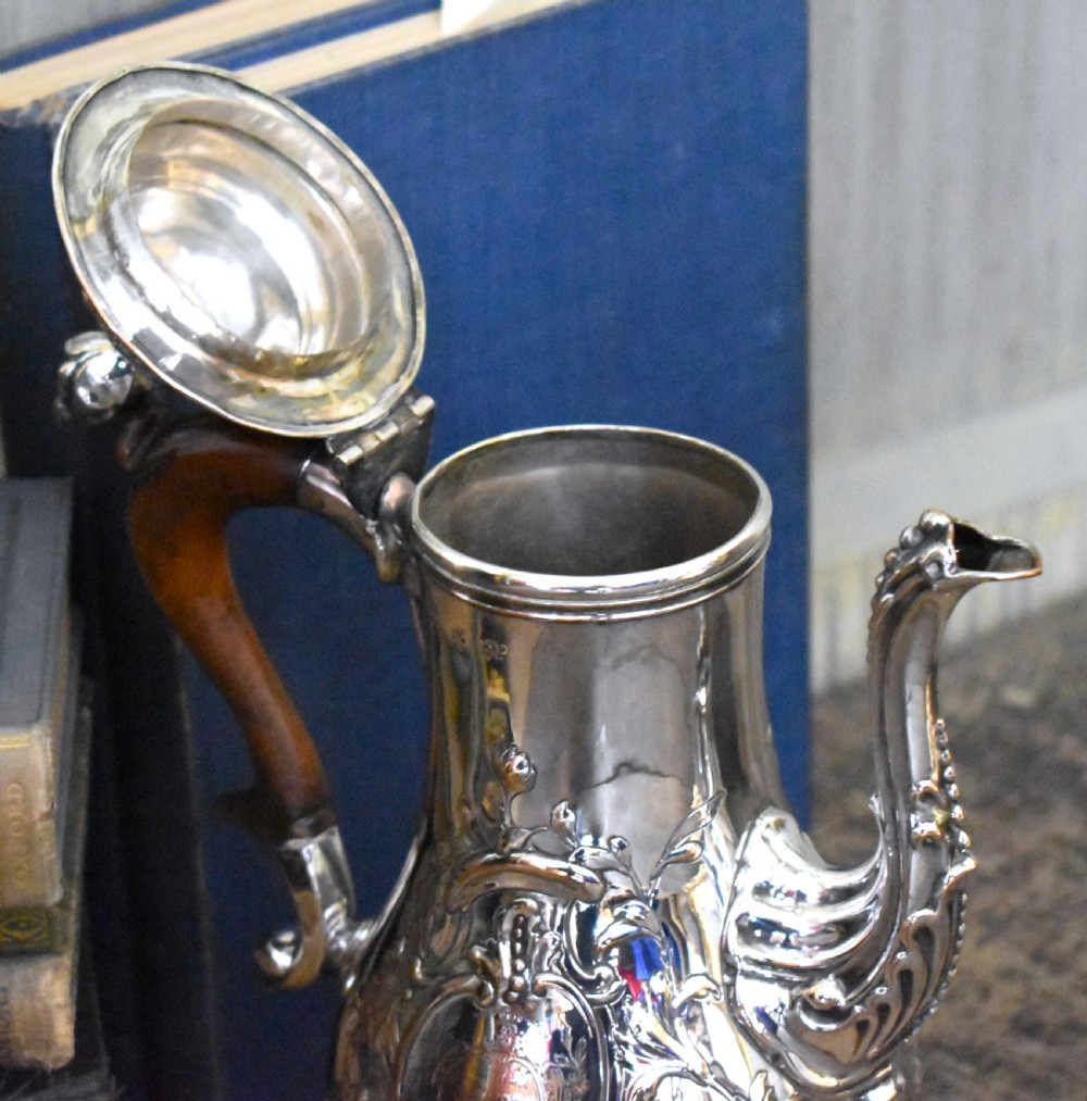 An antique Georgian silver-plated coffee pot featuring repousse floral scrollwork, an engraved cartouche, a carved wooden handle, and a finial lid. View VII