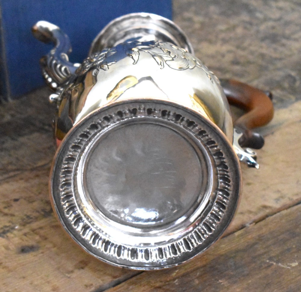 An antique Georgian silver-plated coffee pot featuring repousse floral scrollwork, an engraved cartouche, a carved wooden handle, and a finial lid. View VIII