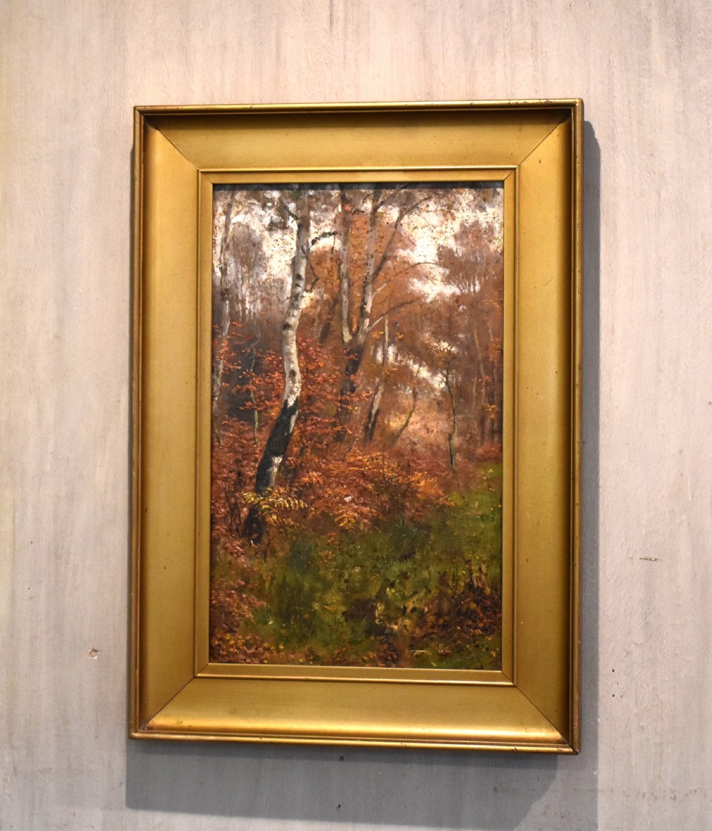 An oil painting depicting an autumnal woodland with birch trees and foliage, set within a wide bevelled gilded frame.