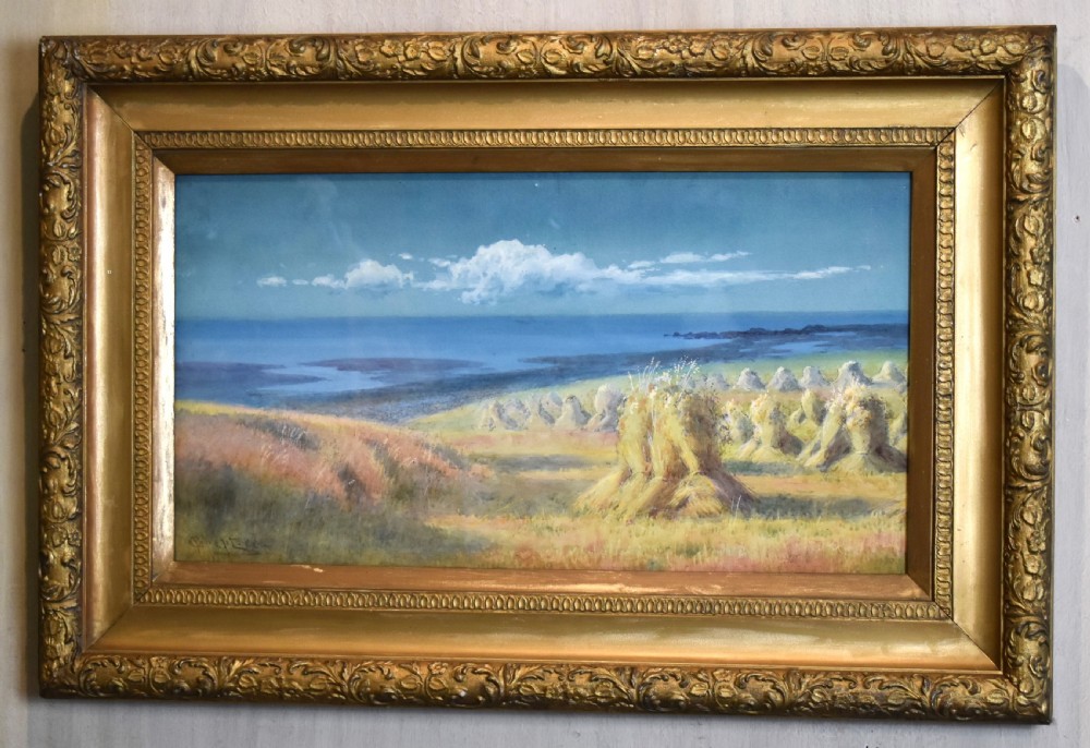 A framed watercolour painting depicting hay stooks in a field overlooking a blue bay under a cloudy sky, presented in a decorative gilt frame. View II