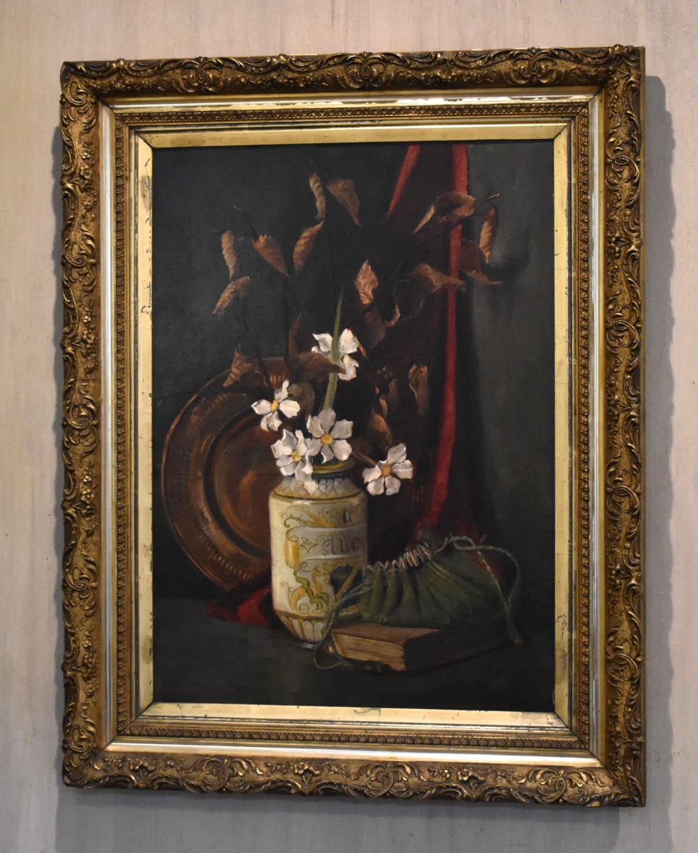 A framed Victorian still life oil painting depicting a ceramic vase with white flowers, a book, and a copper dish against a dark background.