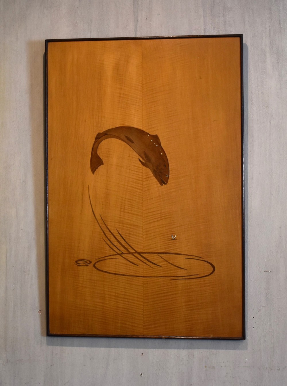 A rectangular honey-toned wood marquetry panel depicting a leaping salmon crafted from inlaid timber veneers.