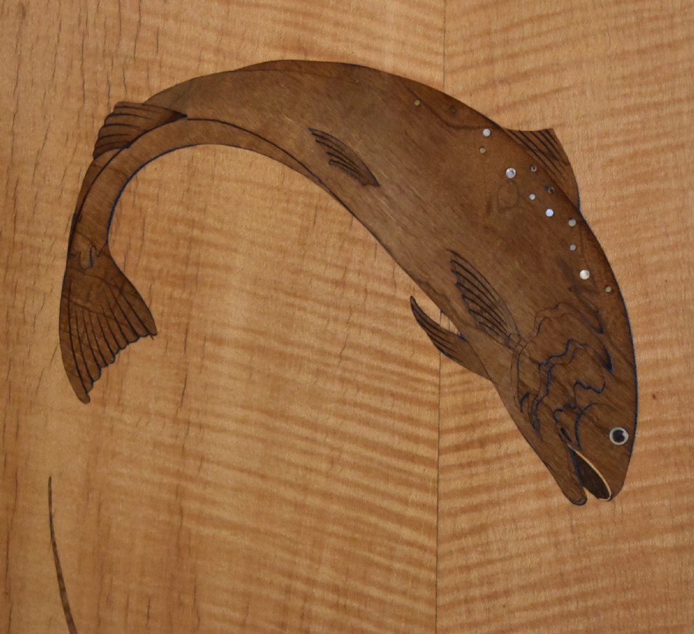 A rectangular honey-toned wood marquetry panel depicting a leaping salmon crafted from inlaid timber veneers. View VI