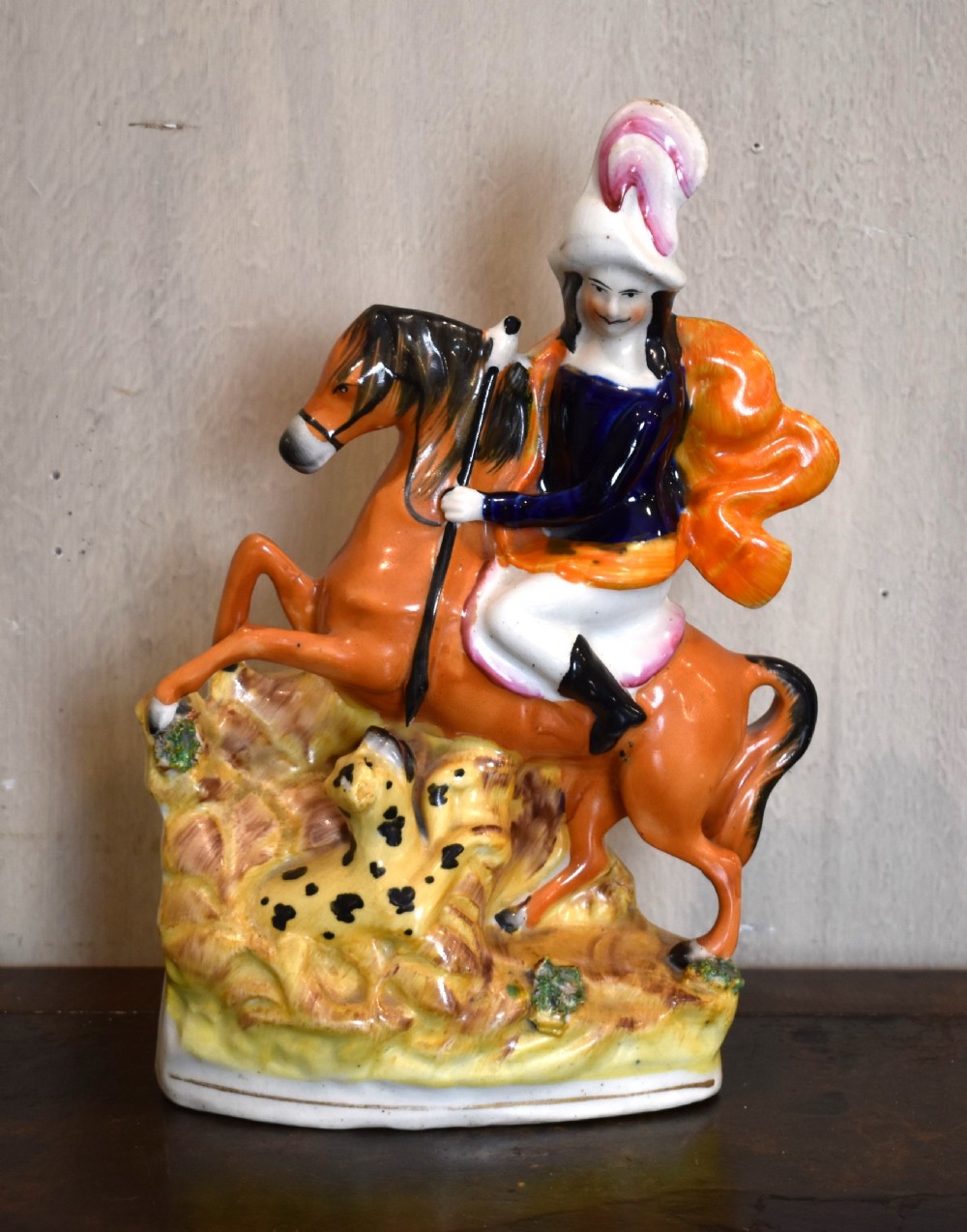 A Victorian Staffordshire earthenware figure depicting an equestrian hunter with a spear riding an orange horse over a spotted leopard on a moulded base.