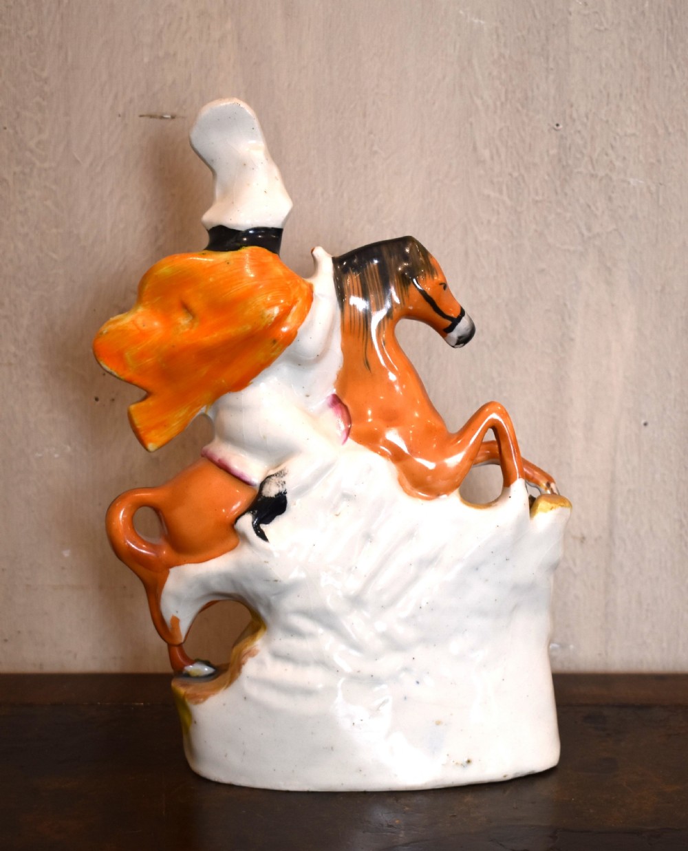 A Victorian Staffordshire earthenware figure depicting an equestrian hunter with a spear riding an orange horse over a spotted leopard on a moulded base. View V