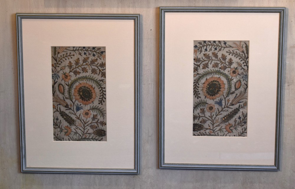 Set of three framed antique needlework panels displaying intricate botanical embroidery, mounted in cream pass-partout and light grey frames. View V
