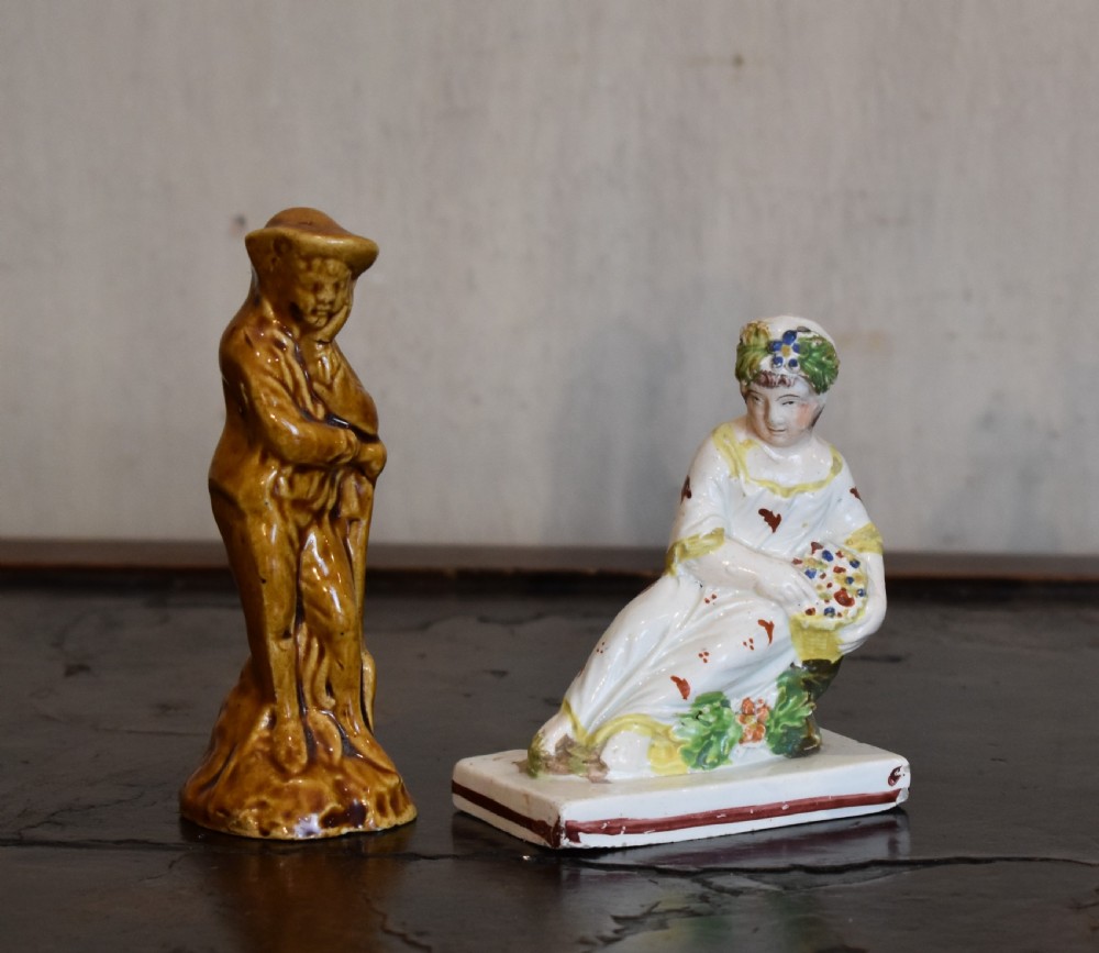 A pair of small early Staffordshire ceramic figures, one standing figure with a brown lead glaze and one seated female figure decorated with colourful hand-painted enamels.