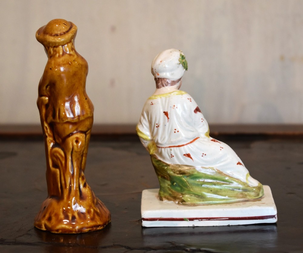 A pair of small early Staffordshire ceramic figures, one standing figure with a brown lead glaze and one seated female figure decorated with colourful hand-painted enamels. View V
