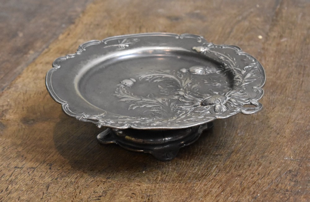 An Art Nouveau Britannia metal tazza with relief carvings of flowers, foliage, and a dragonfly along the scalloped rim. View II