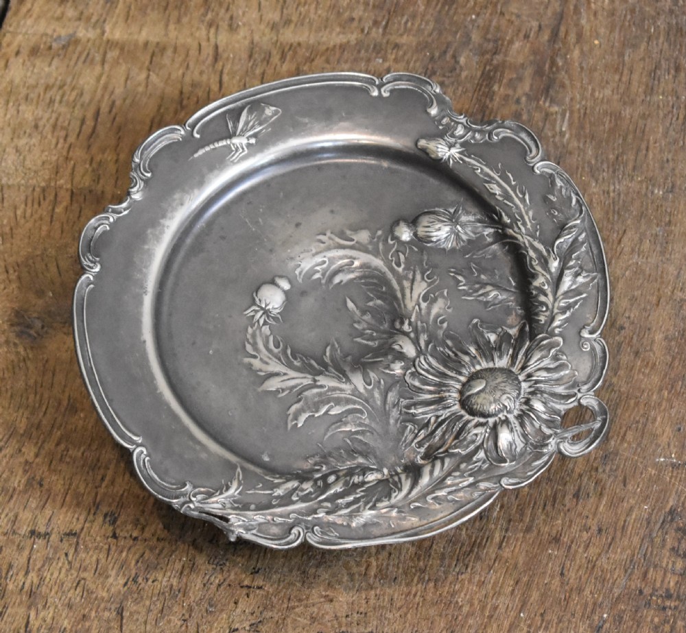 An Art Nouveau Britannia metal tazza with relief carvings of flowers, foliage, and a dragonfly along the scalloped rim. View III