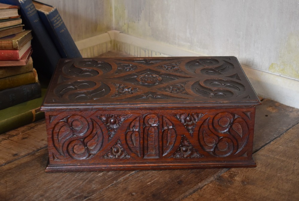A rectangular dark carved oak box featuring intricate Gothic Revival relief carvings on the top lid and front panels.