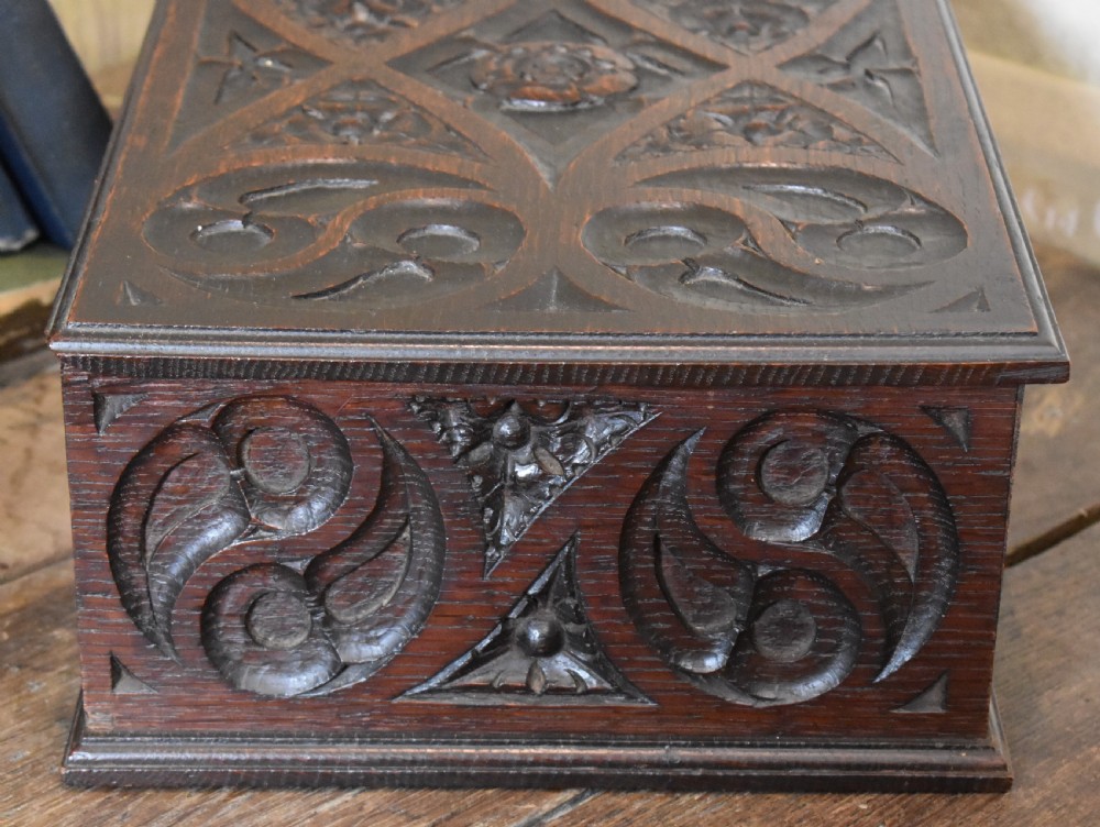 A rectangular dark carved oak box featuring intricate Gothic Revival relief carvings on the top lid and front panels. View V