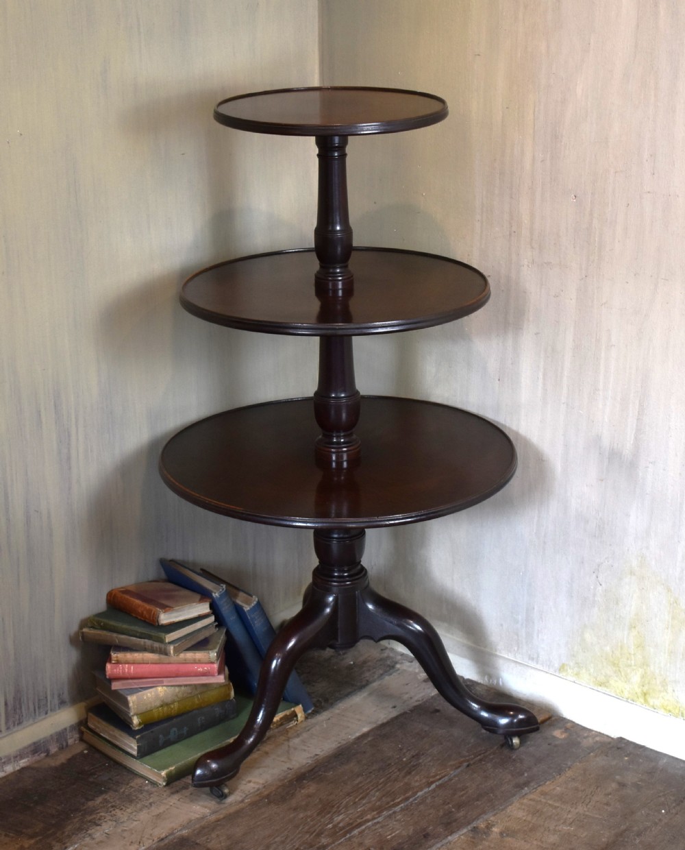 A Georgian mahogany three-tiered dumb waiter with graduated circular trays on a central turned stem supported by tripod cabriole legs with brass castors.