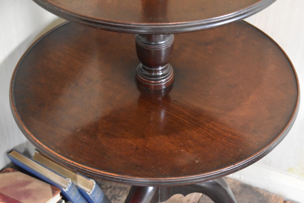 A Georgian mahogany three-tiered dumb waiter with graduated circular trays on a central turned stem supported by tripod cabriole legs with brass castors. View II