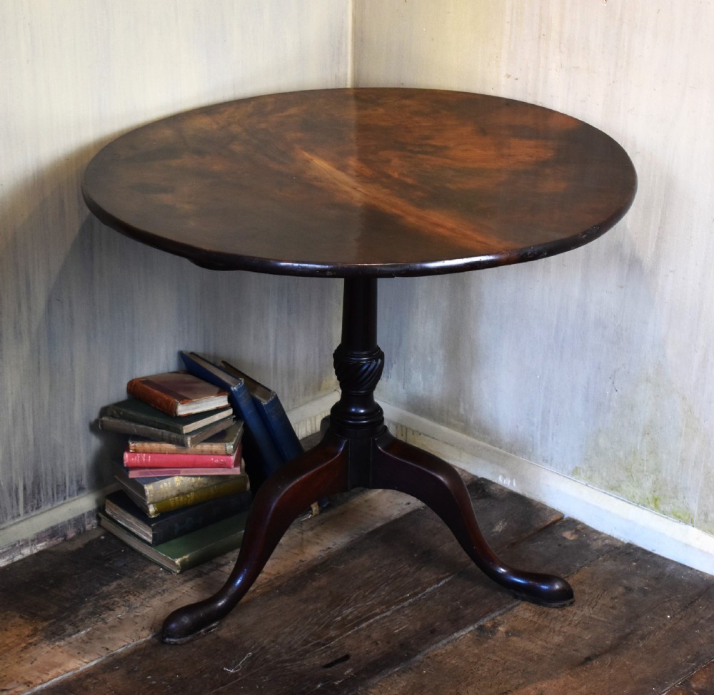 An 18th-century Georgian mahogany tilt-top table featuring a circular surface, a turned central pedestal, and three splayed cabriole legs.