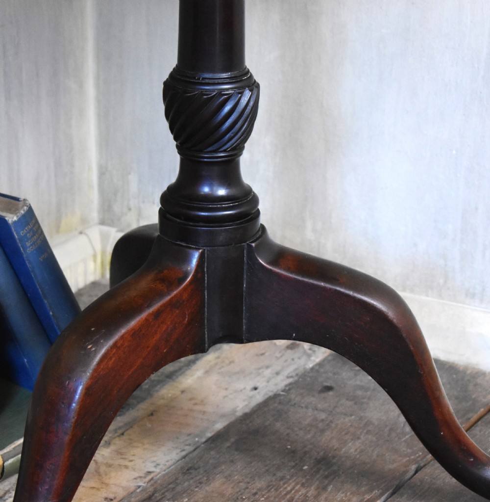 An 18th-century Georgian mahogany tilt-top table featuring a circular surface, a turned central pedestal, and three splayed cabriole legs. View V
