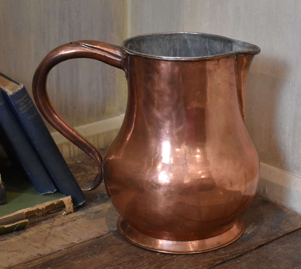 A large Georgian hand-hammered copper jug featuring a rounded baluster body, shaped pouring spout, heavy looped handle, and tin-lined interior.