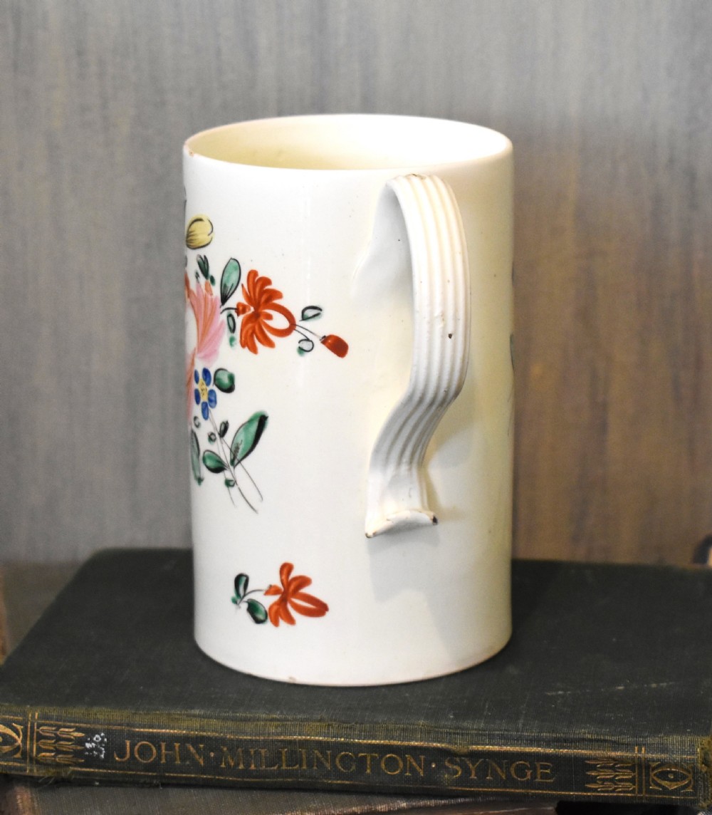 A cylindrical creamware ceramic tankard decorated with hand-painted polychrome floral motifs and a loop handle. View II