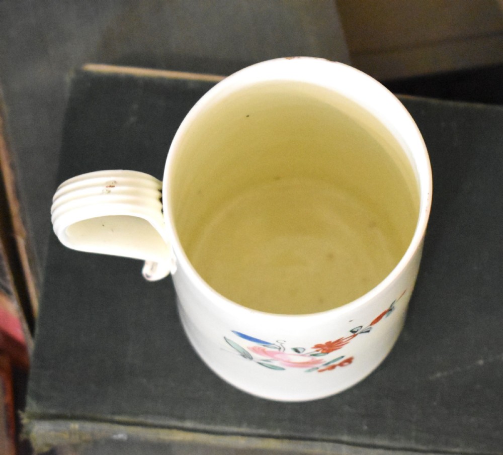 A cylindrical creamware ceramic tankard decorated with hand-painted polychrome floral motifs and a loop handle. View V