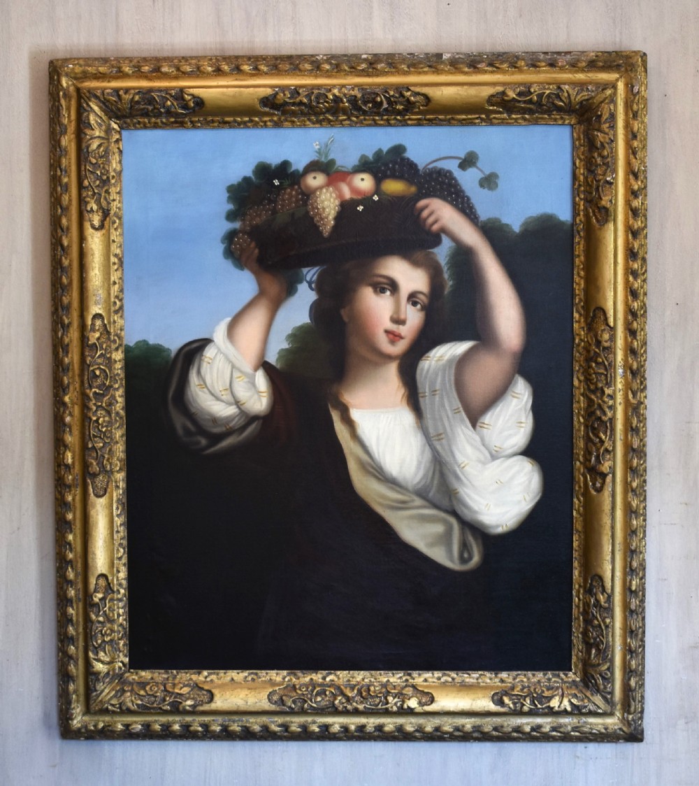 A portrait oil painting depicting a young woman carrying a basket of fruit on her head, set within an ornate carved gilt wood frame. View II
