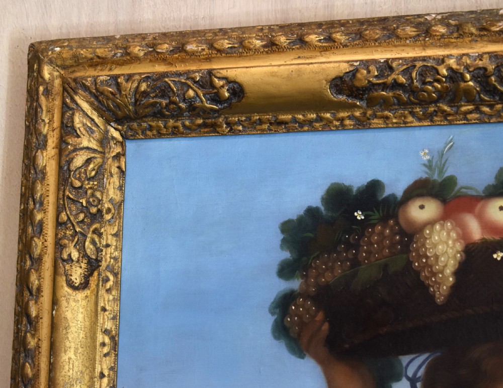 A portrait oil painting depicting a young woman carrying a basket of fruit on her head, set within an ornate carved gilt wood frame. View VI