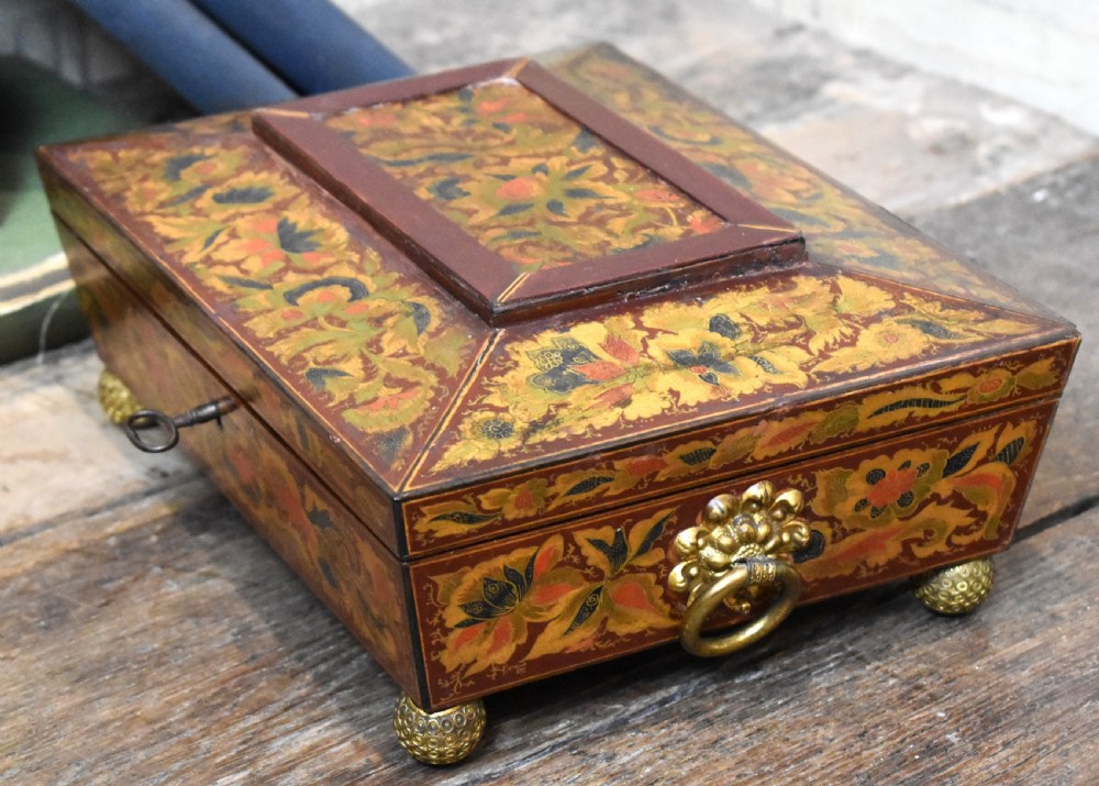 A rectangular Regency period wooden box featuring intricate botanical penwork decoration, brass ring handles, and ball feet. View III