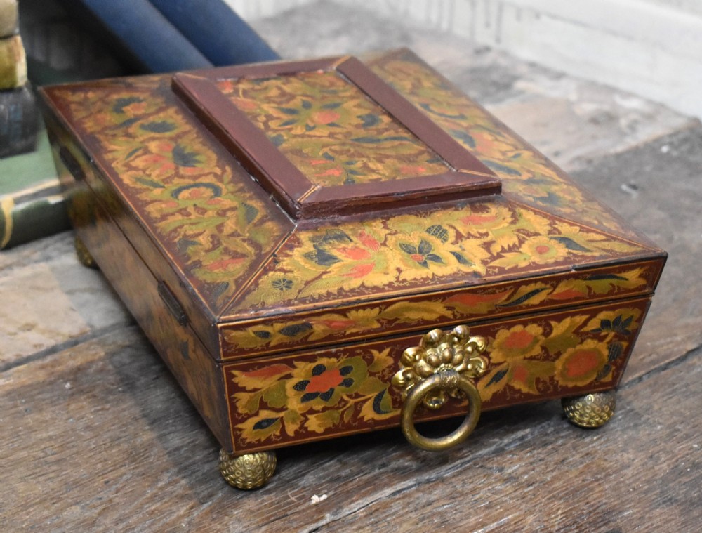 A rectangular Regency period wooden box featuring intricate botanical penwork decoration, brass ring handles, and ball feet. View VI