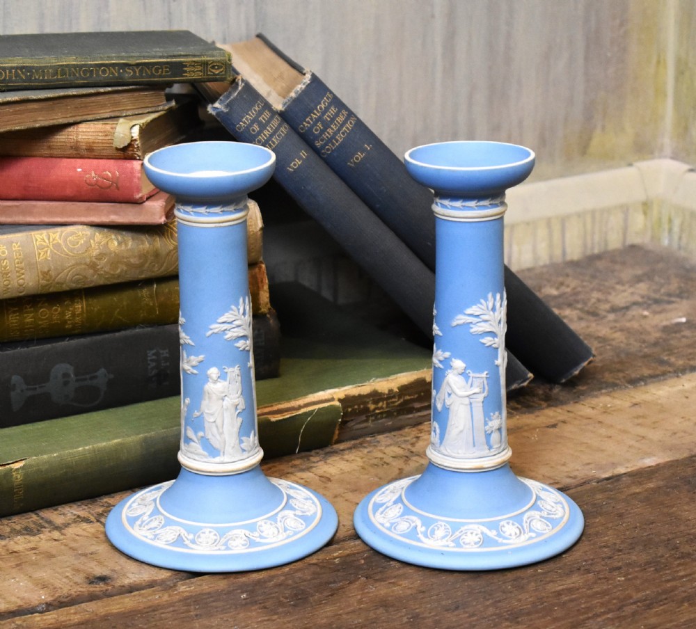 A pair of light blue Wedgwood jasperware candlesticks featuring white neoclassical bas-relief figures and classical floral bands on circular bases.