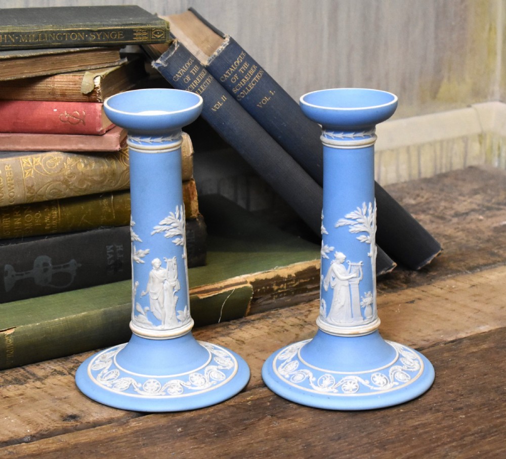 A pair of light blue Wedgwood jasperware candlesticks featuring white neoclassical bas-relief figures and classical floral bands on circular bases. View II