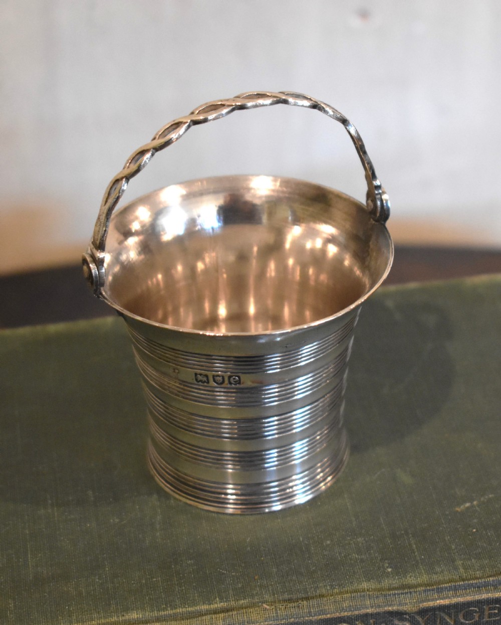 A solid silver miniature bucket pail featuring horizontal reeded detailing, visible hallmarks on the exterior, and a twisted swing handle. View II