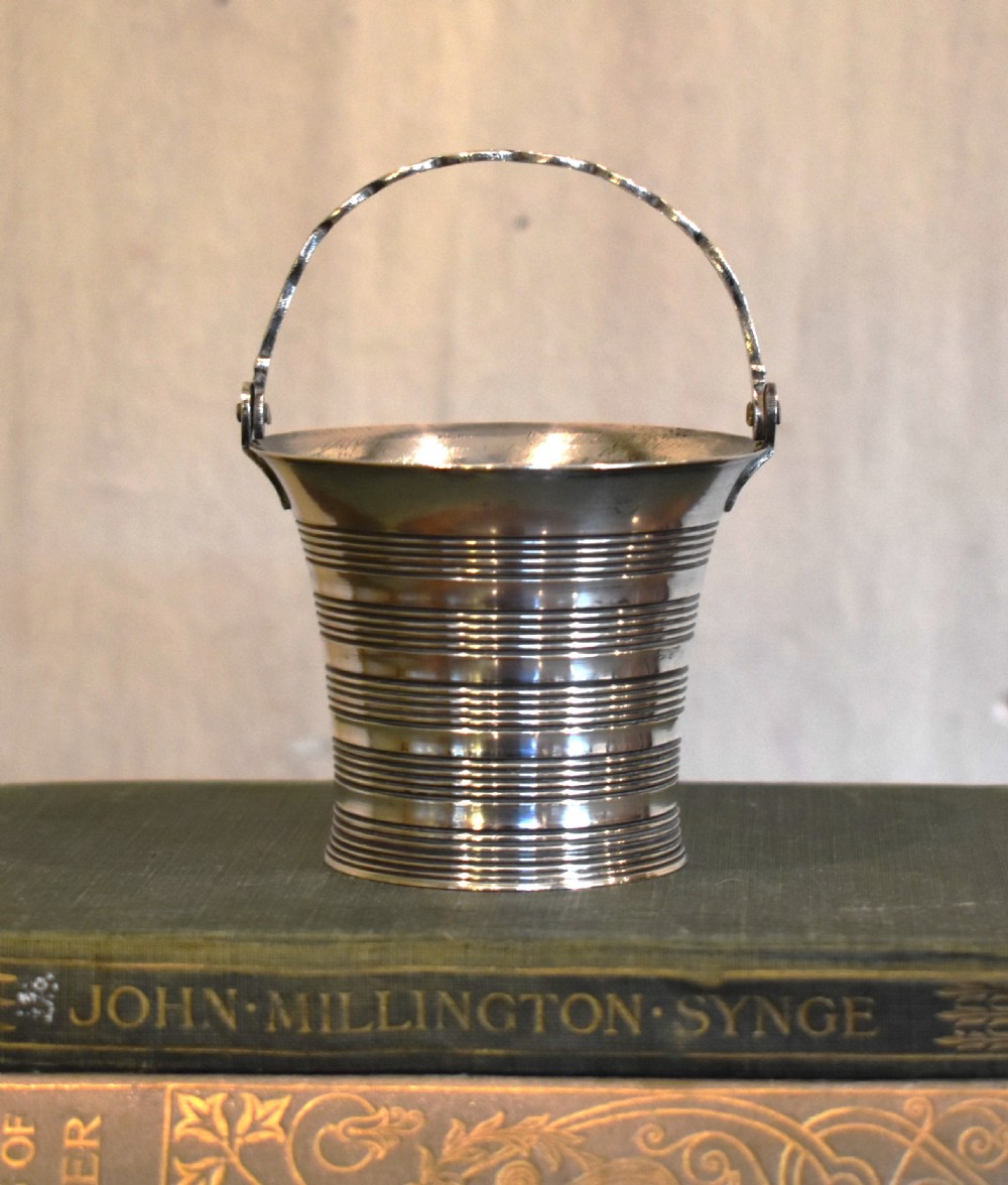 A solid silver miniature bucket pail featuring horizontal reeded detailing, visible hallmarks on the exterior, and a twisted swing handle. View III