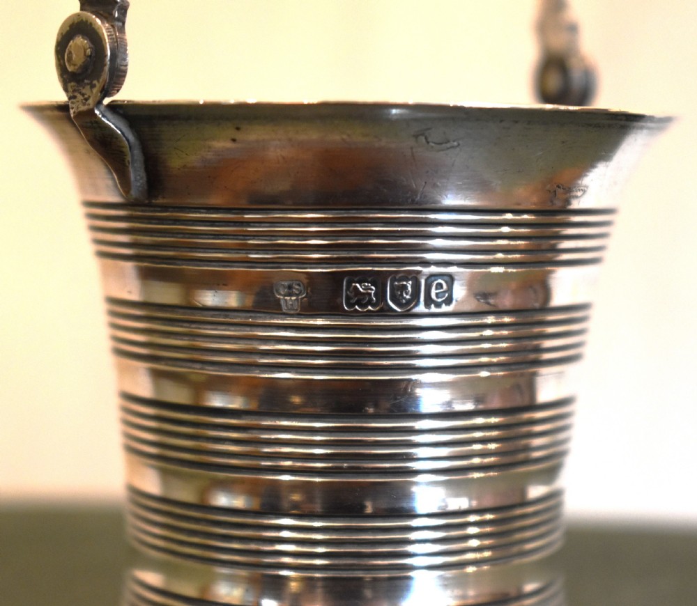A solid silver miniature bucket pail featuring horizontal reeded detailing, visible hallmarks on the exterior, and a twisted swing handle. View IV