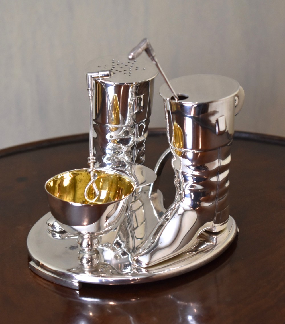 A silver-plated novelty equestrian cruet set featuring a riding boot mustard pot with a spur handle, a cap pepper shaker, and a gilt-lined salt cellar on a fitted tray. View II