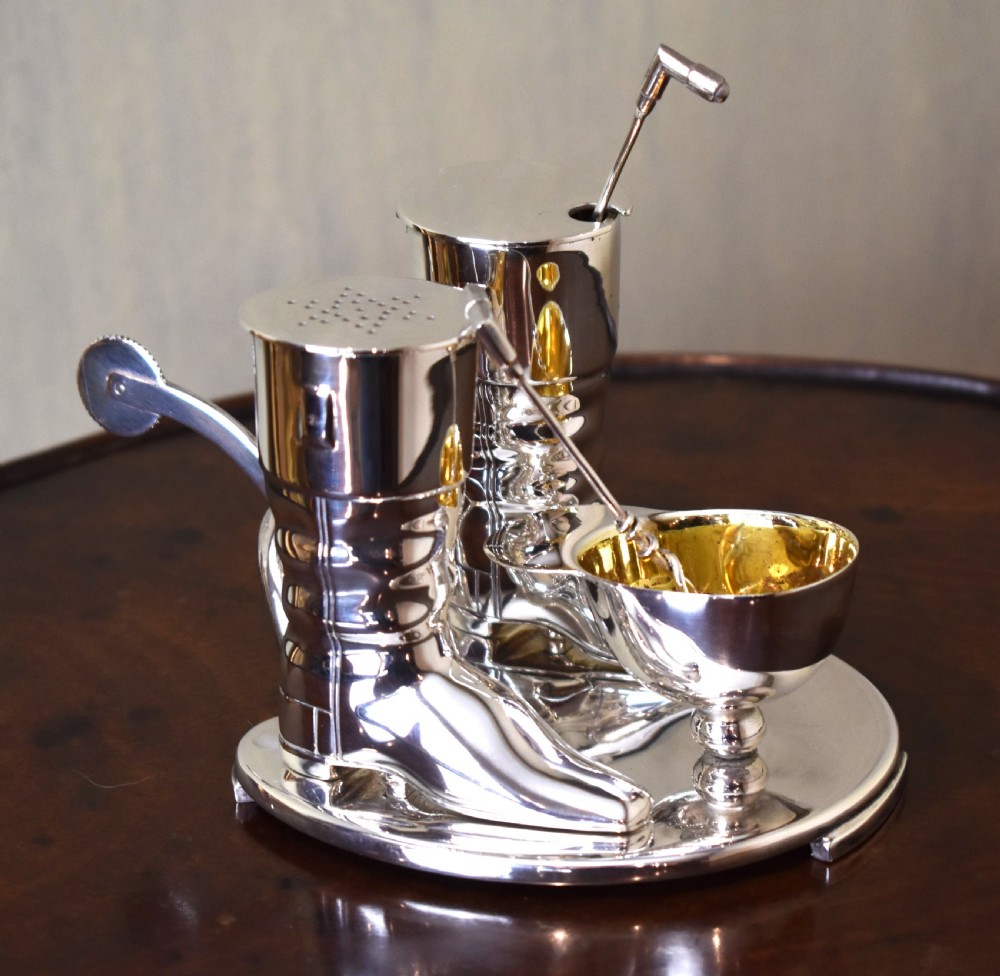 A silver-plated novelty equestrian cruet set featuring a riding boot mustard pot with a spur handle, a cap pepper shaker, and a gilt-lined salt cellar on a fitted tray. View VI