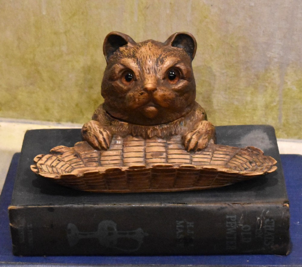 A carved wooden Black Forest inkwell featuring the detailed head of a cat with glass eyes positioned behind a basketweave pen tray.