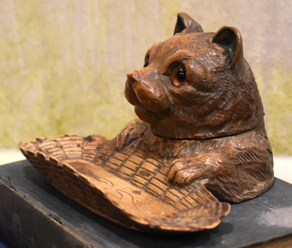 A carved wooden Black Forest inkwell featuring the detailed head of a cat with glass eyes positioned behind a basketweave pen tray. View V
