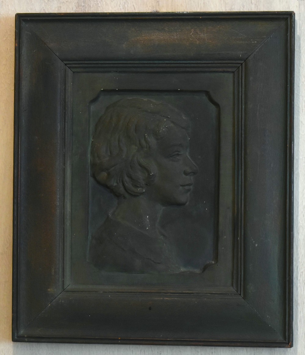 A dark bronzed plaster relief sculpture showing a profile portrait of a young person in a moulded rectangular frame. View II
