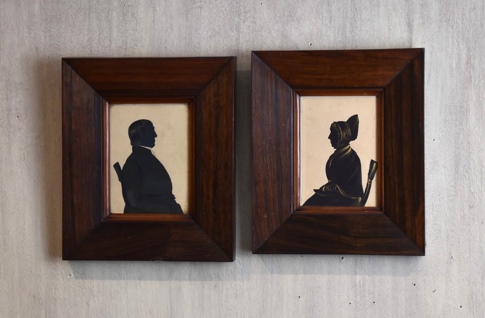 A pair of framed Victorian profile silhouettes depicting a man and a woman in polished dark wood frames.