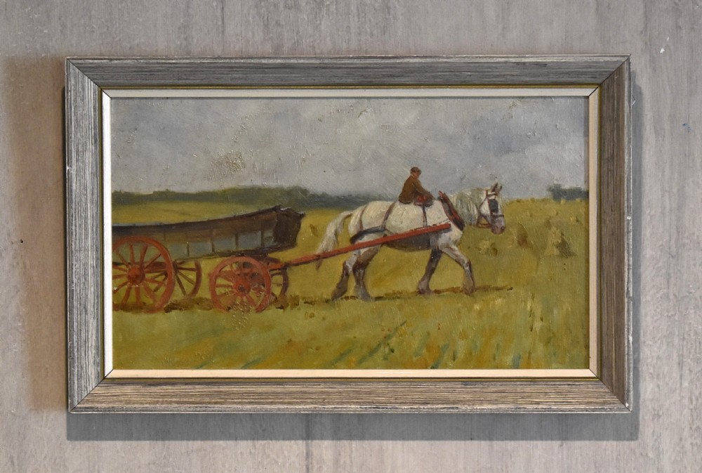 A framed horizontal oil painting depicting a grey draft horse pulling a brown wooden cart across a green field under a cloudy grey sky.