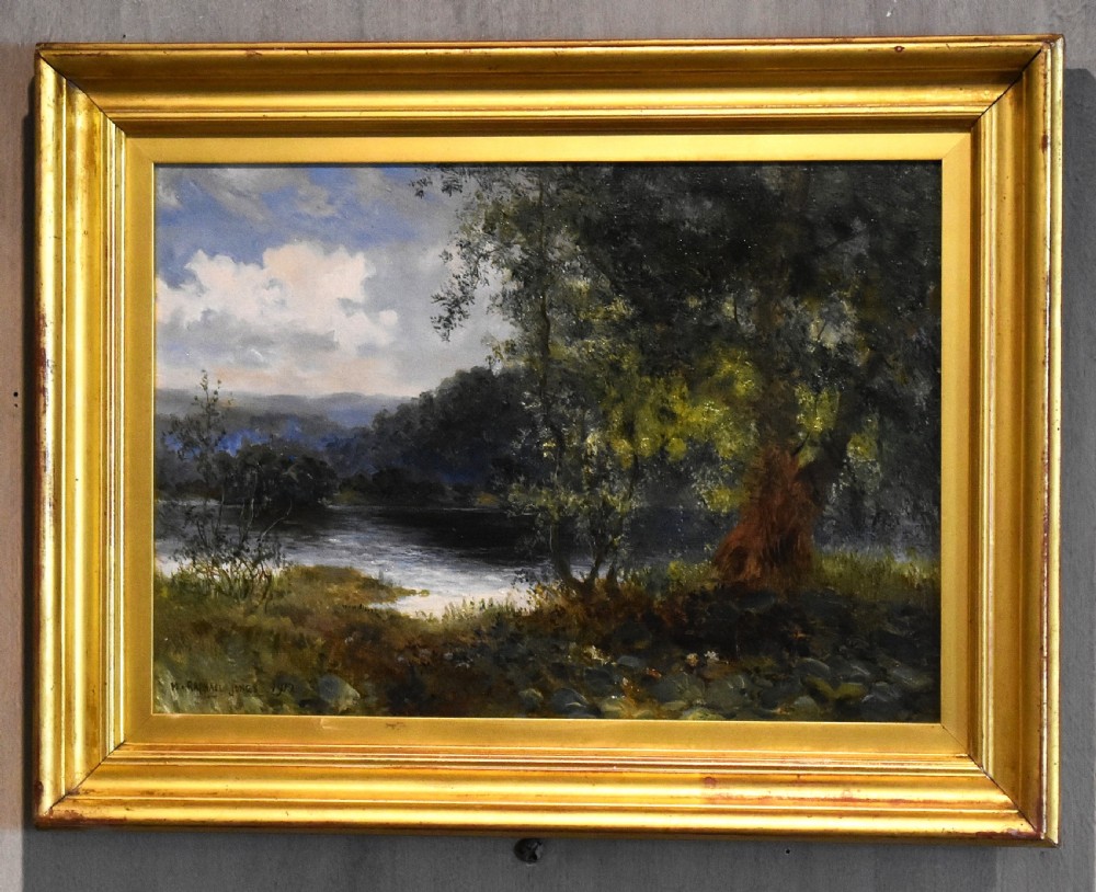 A framed oil painting depicting a tranquil river scene with leafy green trees, distant hills, and a cloudy blue sky, encased in a gold gilded wooden frame. View II