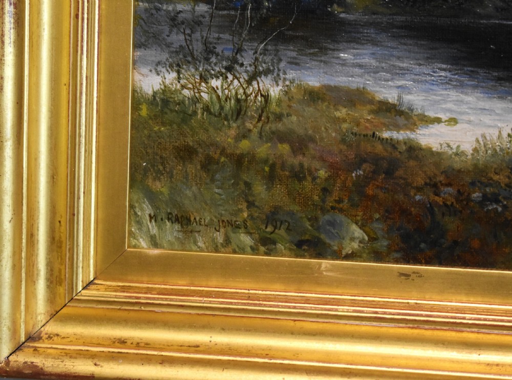 A framed oil painting depicting a tranquil river scene with leafy green trees, distant hills, and a cloudy blue sky, encased in a gold gilded wooden frame. View V