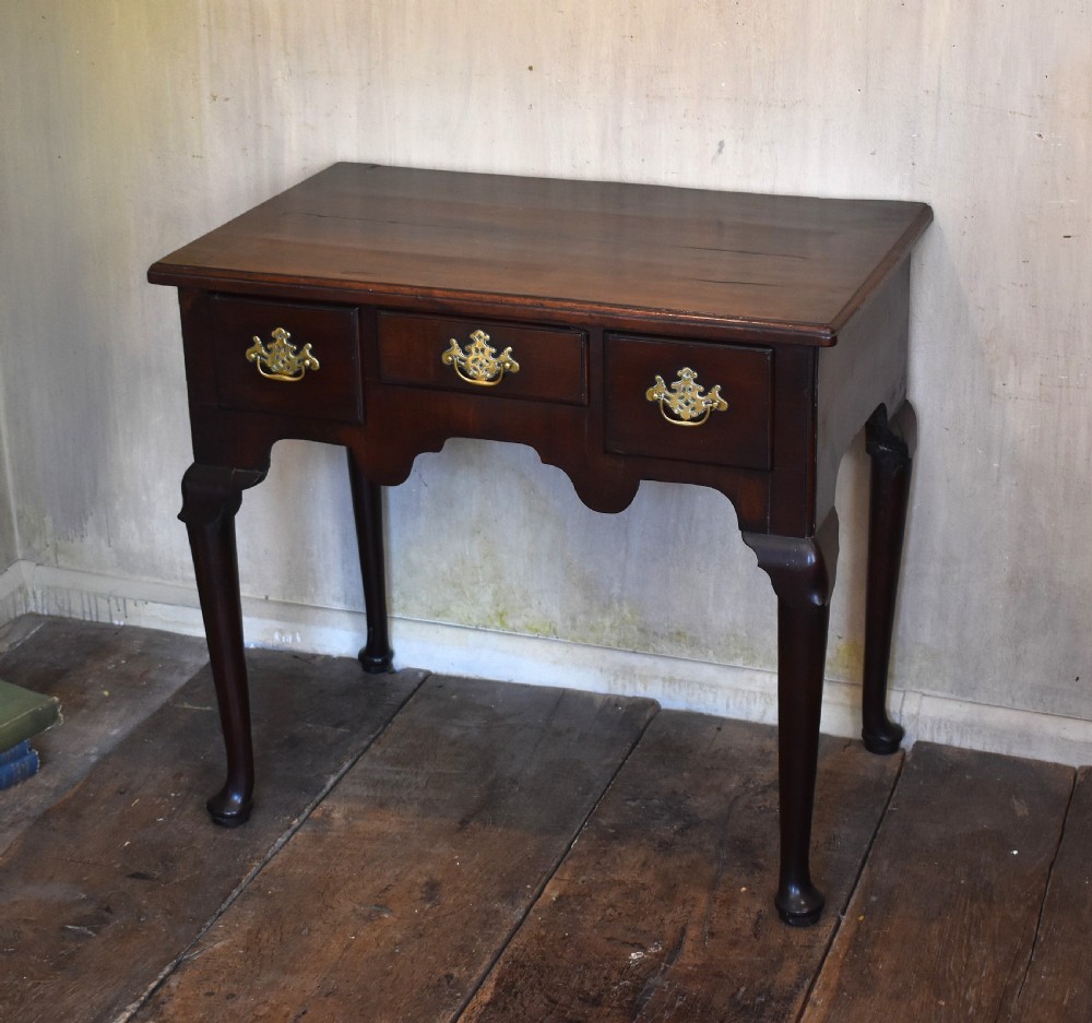 A Georgian mahogany lowboy featuring three drawers fitted with pierced brass batwing handles, a shaped apron, and pad feet on cabriole legs.
