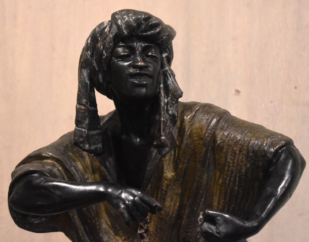 A patinated bronze sculpture depicting an Arab merchant standing over a small wooden box and holding items in draped robes. View IV